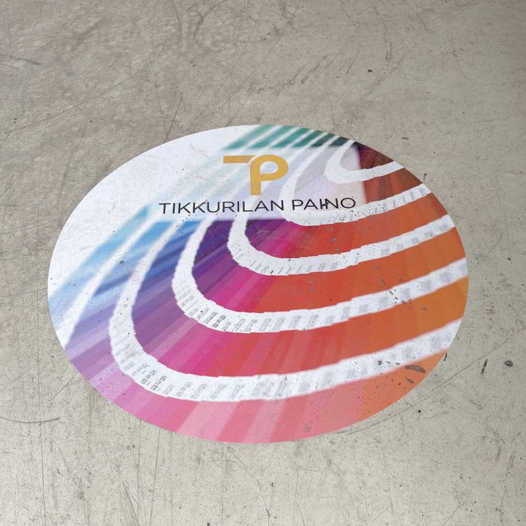Lattiassa näkyvä värikäs mainostarra, jossa Tikkurilan Painon logo ja liukuestepinta. Anti slip -laminointi lisää myös lattiatarran kulutuksen kestävyyttä.